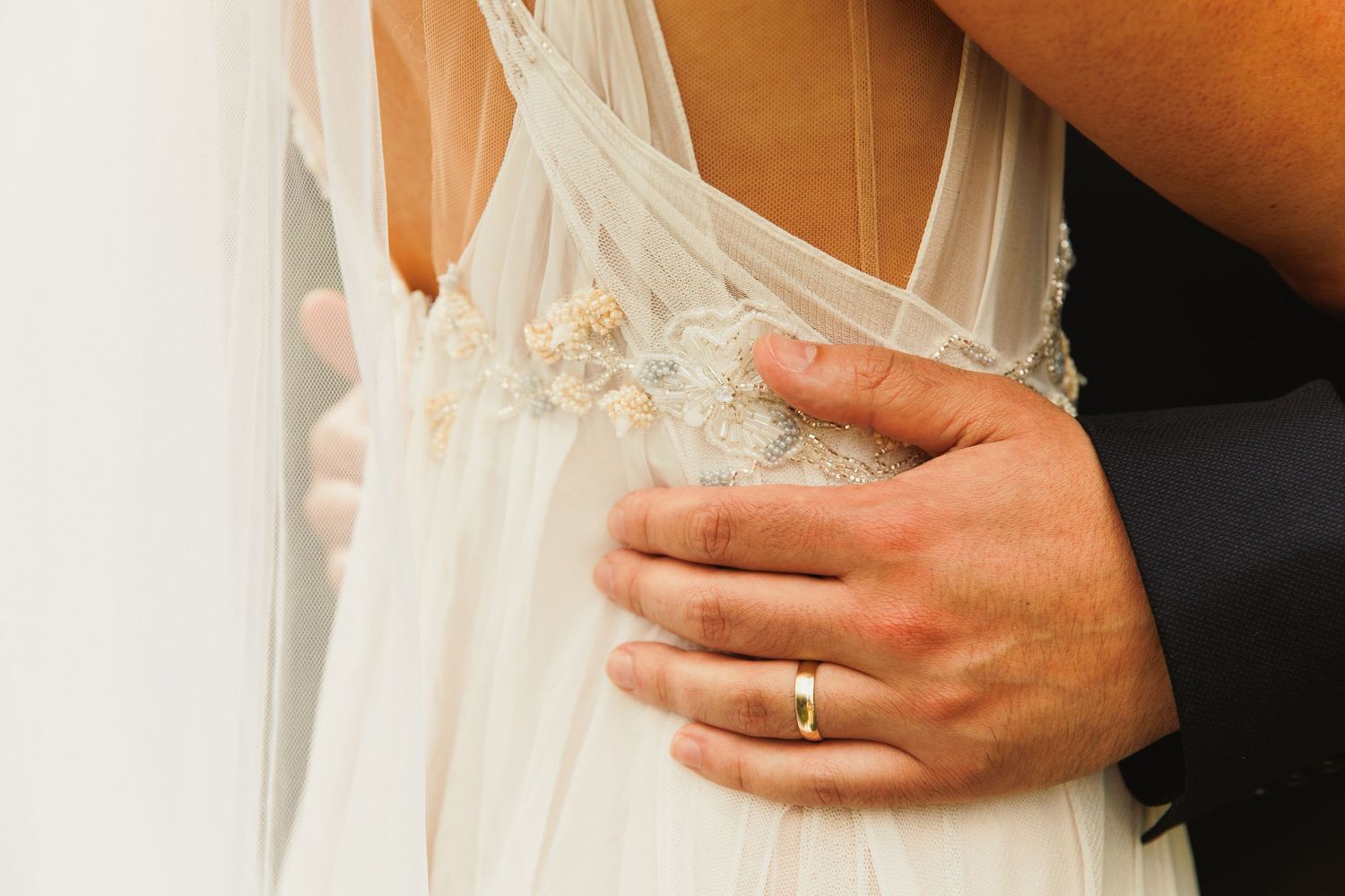 Close-up details of a wedding dress and hands showing delicate lace and ring details.