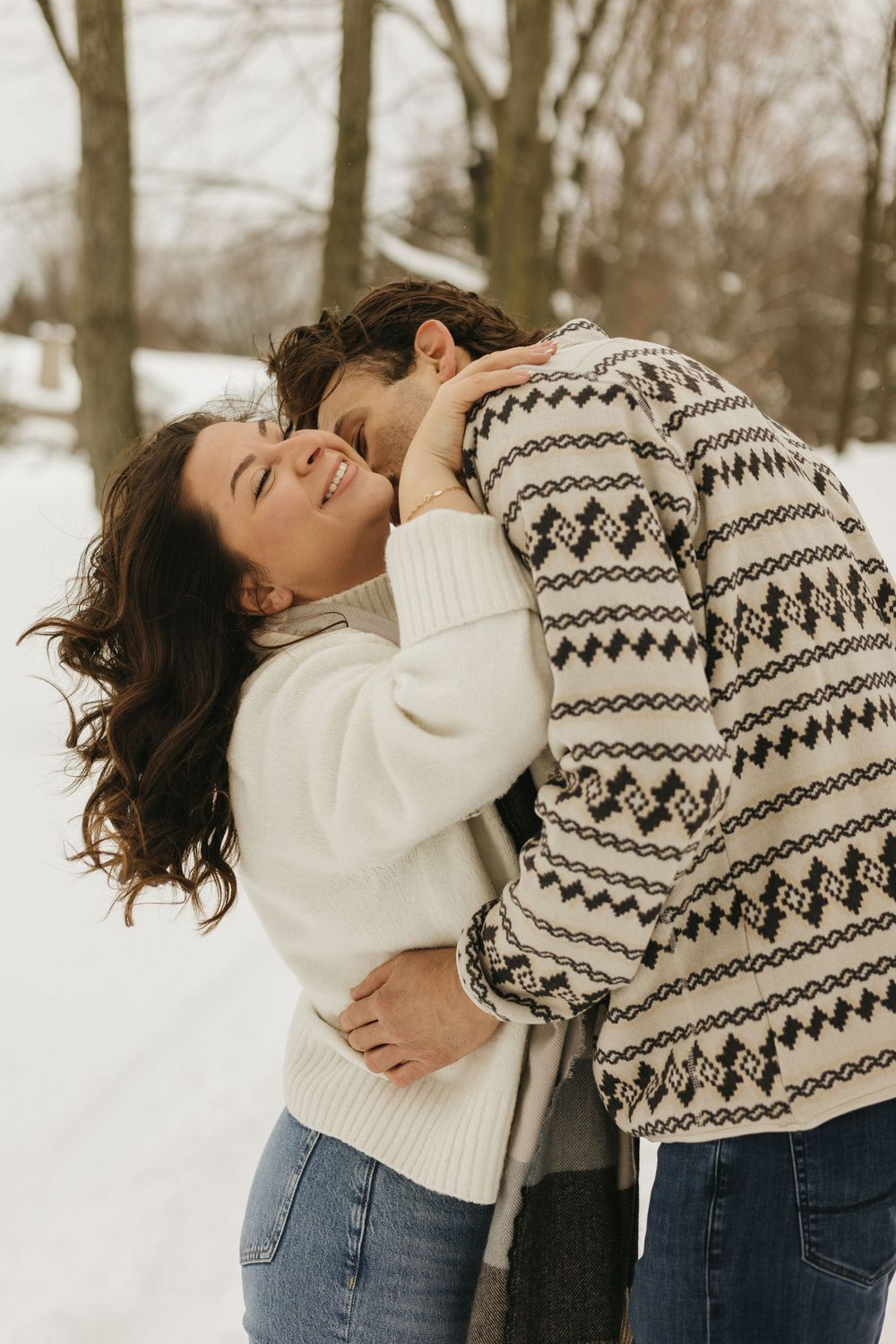 Couple in winter attire sharing an intimate embrace against a snowy backdrop.
