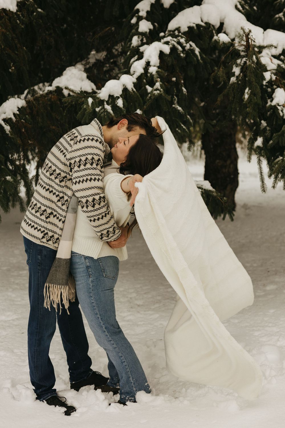 Playful couple creating snow angels while lying in fresh powder snow during winter.