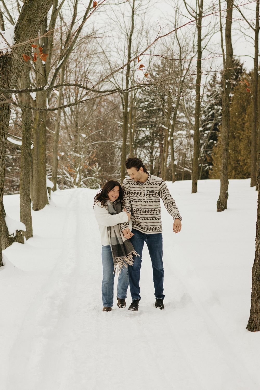 Couple walking together through a snowy winter forest path, bundled up in warm clothing.