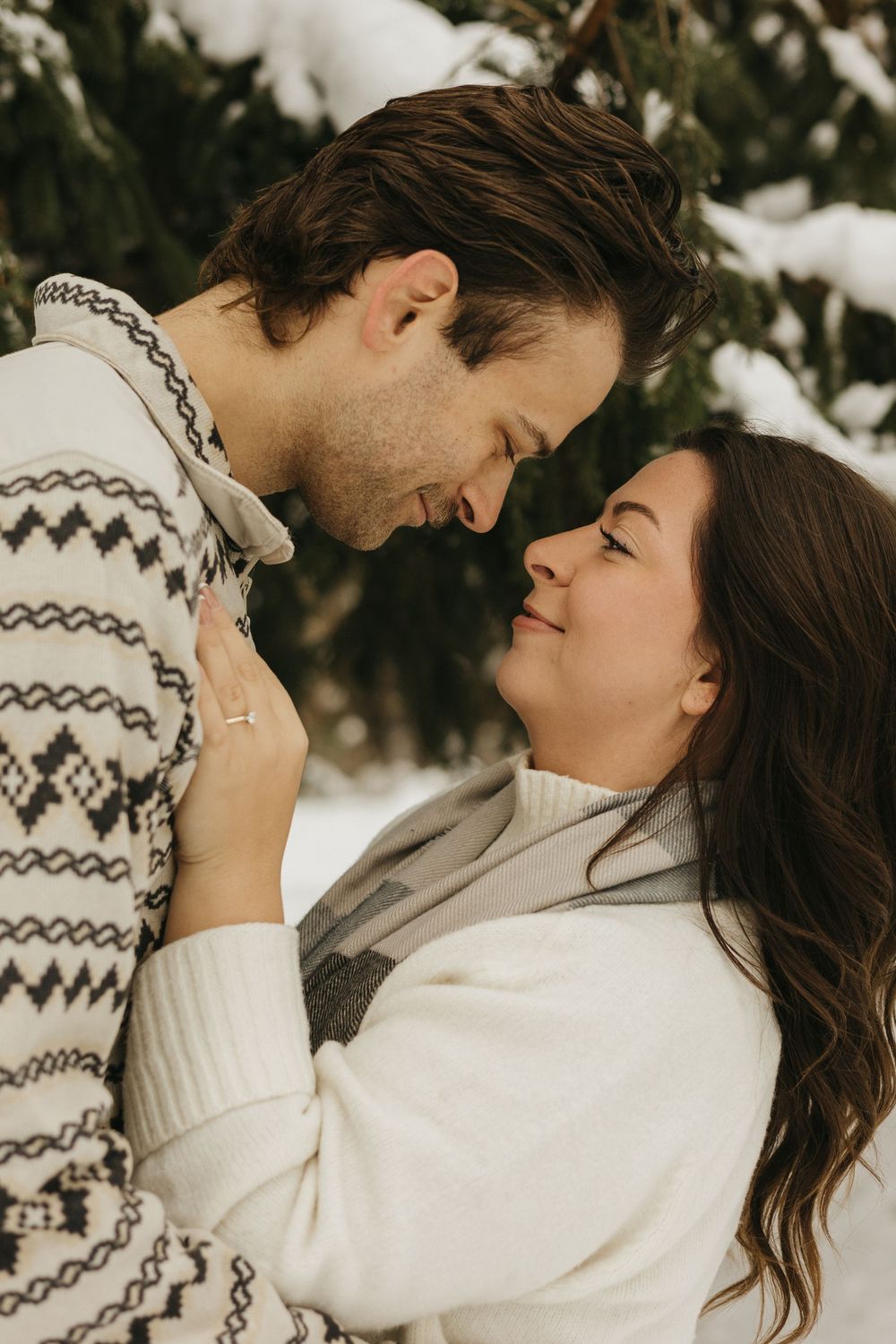 A romantic winter photoshoot showing a couple in white sweaters embracing in the snow.