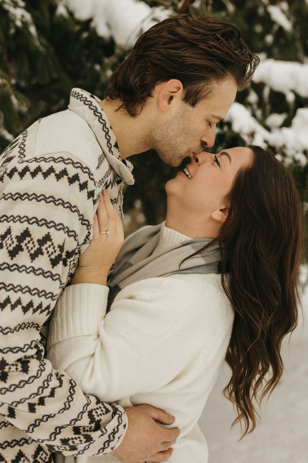 A romantic winter scene with a couple embracing in the snow while wearing cozy sweaters.