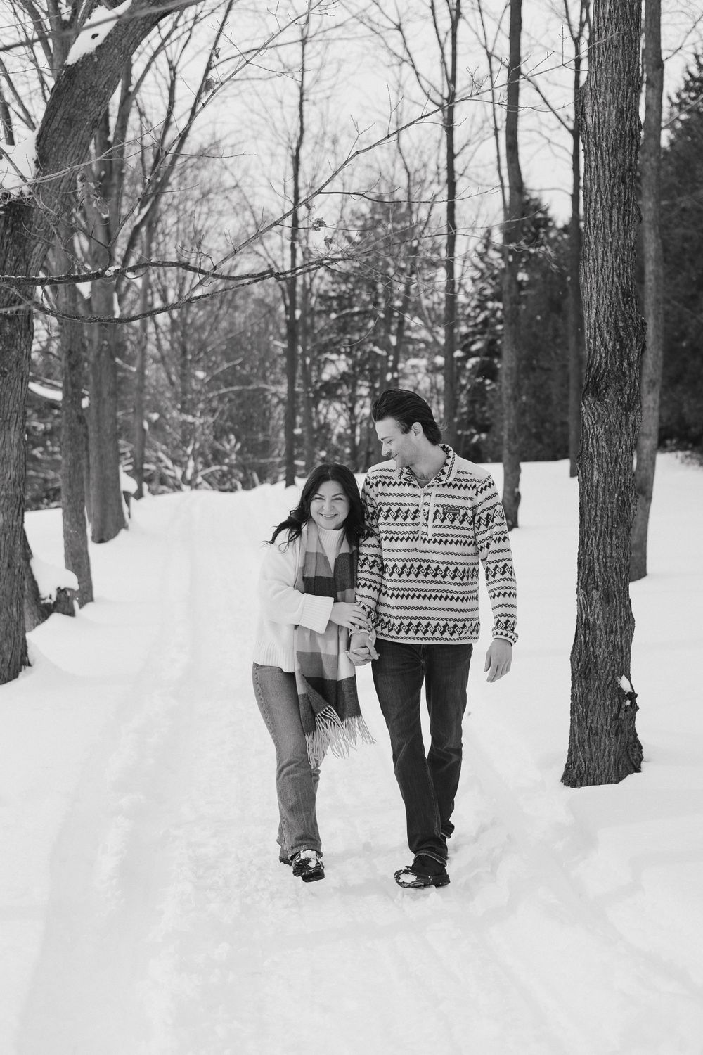 People enjoying a snowy day in a wooded area wearing winter clothing and patterned sweaters.