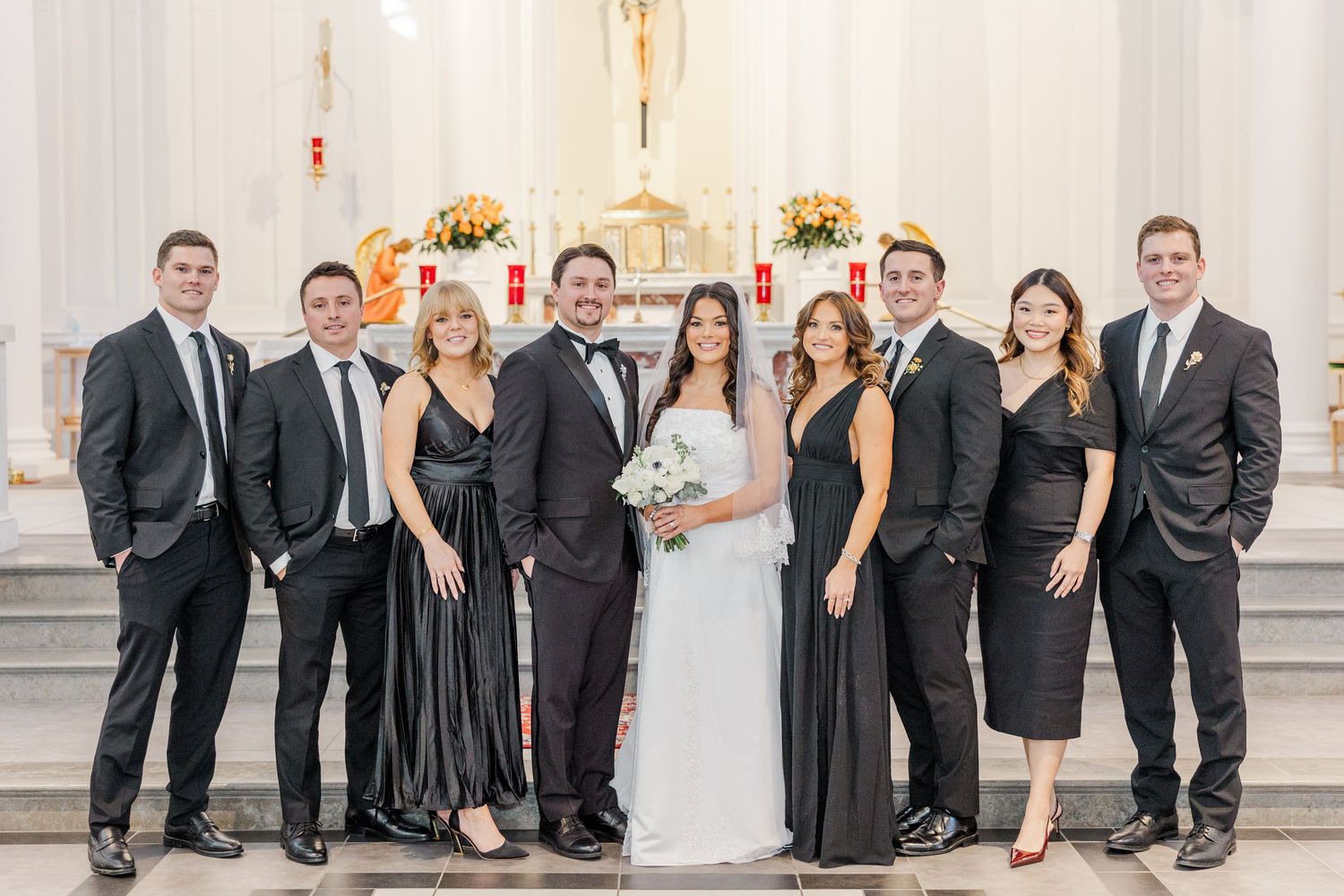 Wedding party in formal black and white attire poses together in an elegant white room with columns.