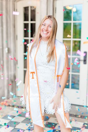 Joyful celebration scene with confetti falling around a person in white lace dress and orange vest against a bright backdrop.