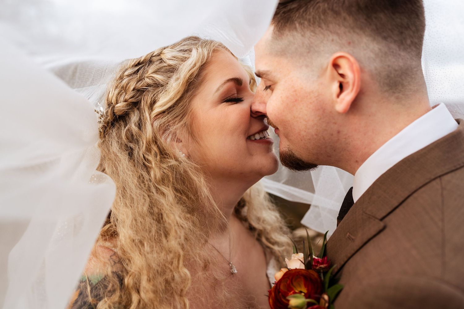 A romantic wedding couple embraces under a flowing white veil during their intimate ceremony celebration.