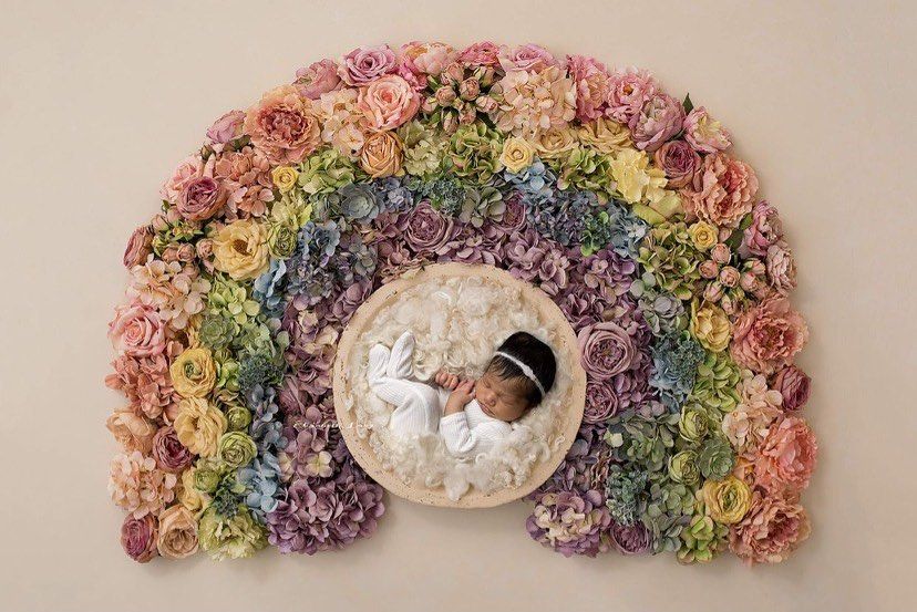 A rainbow-colored floral wreath made of dried hydrangeas creates an elegant curved arrangement on a neutral background.