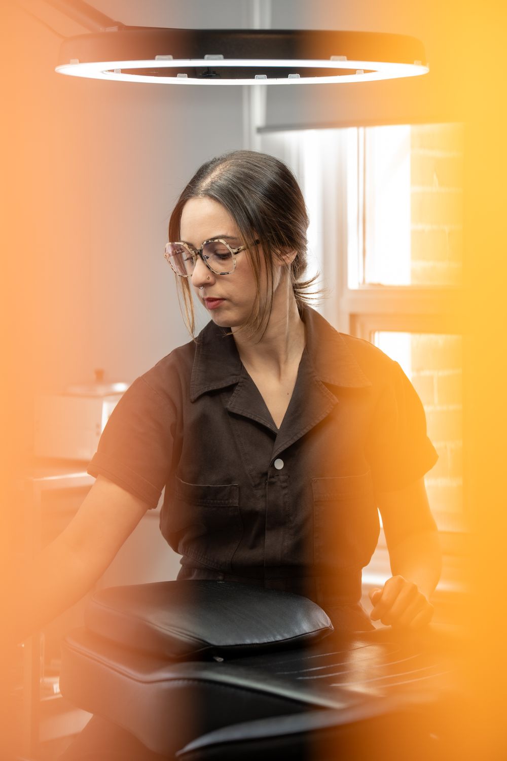 Female professional wearing glasses working at desk under circular ring light in modern salon.
