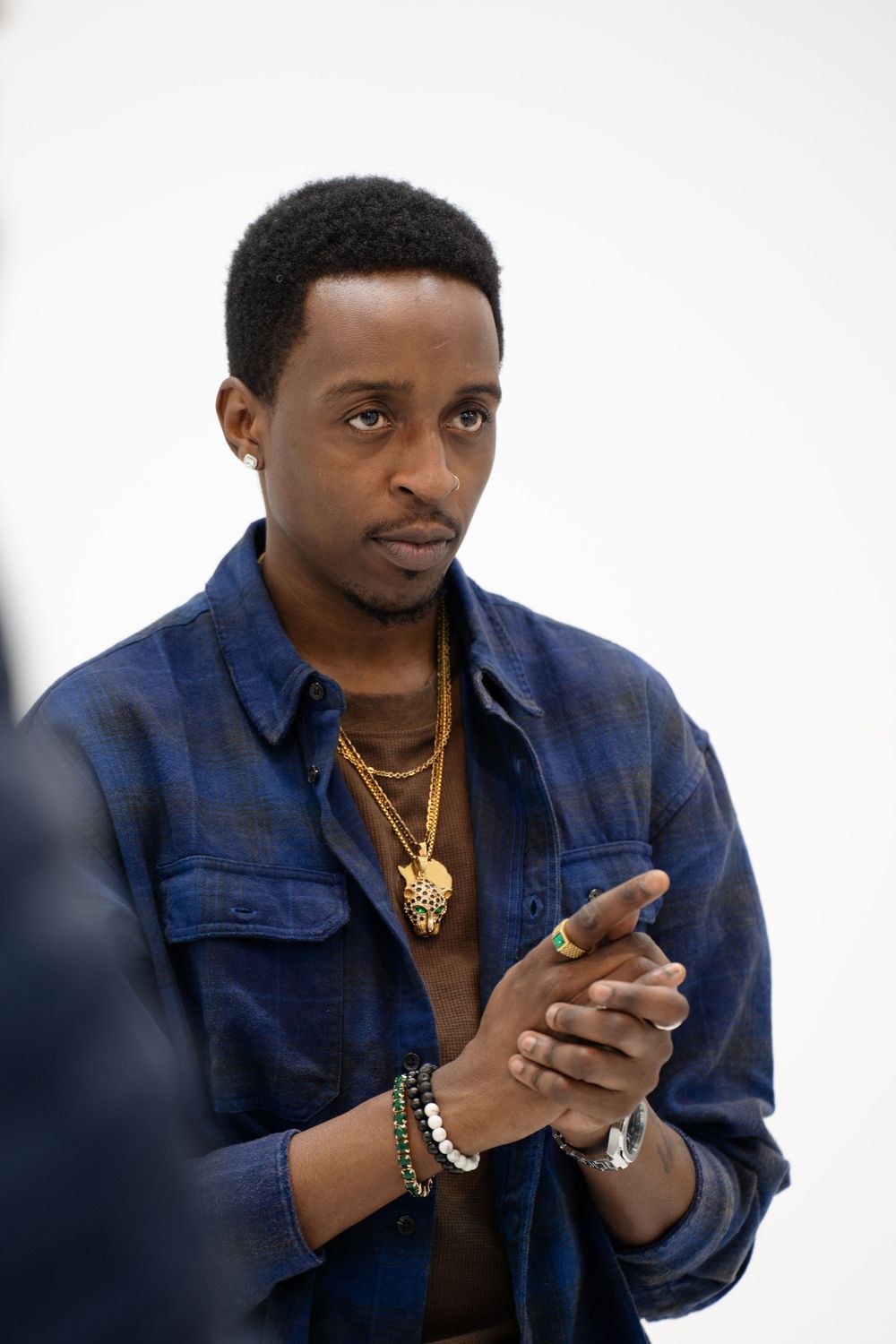 Person in navy blue jacket and gold necklace looking at mobile phone against white background.
