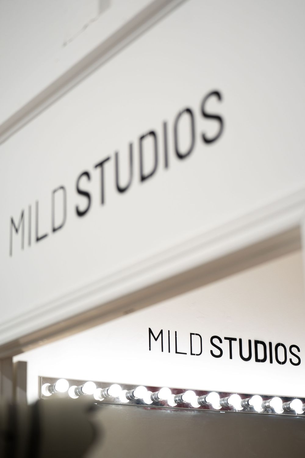 White 'MILD STUDIOS' signage illuminated by a row of small lights against a clean modern wall.