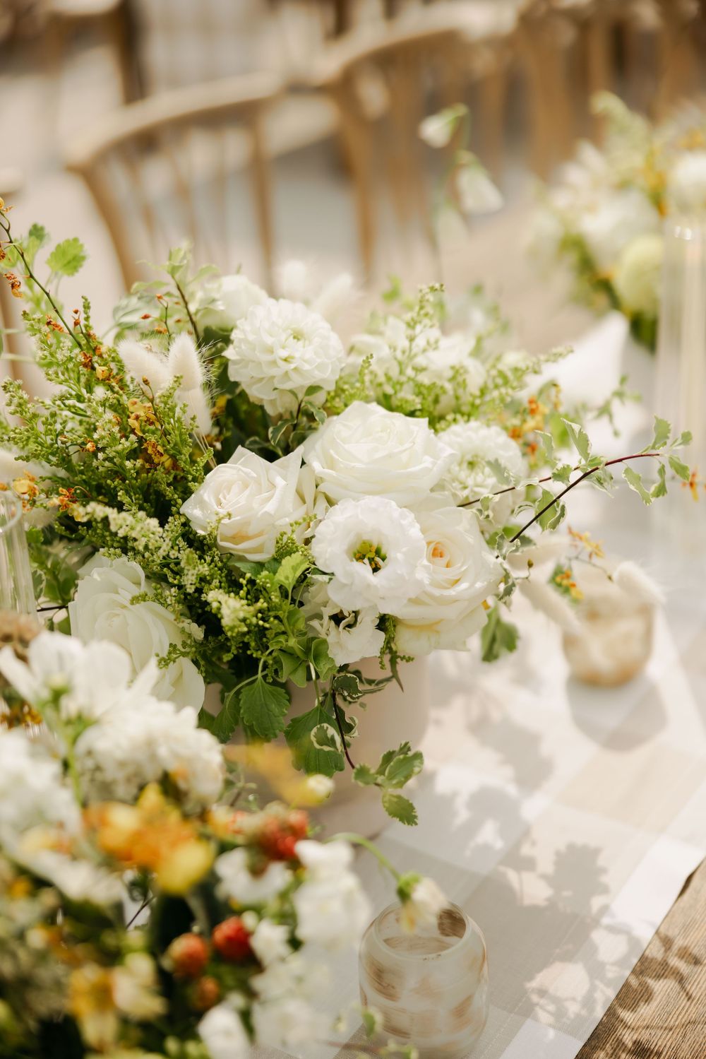 Elegant wedding floral arrangements featuring white roses and delicate greenery on a light-colored tablecloth.