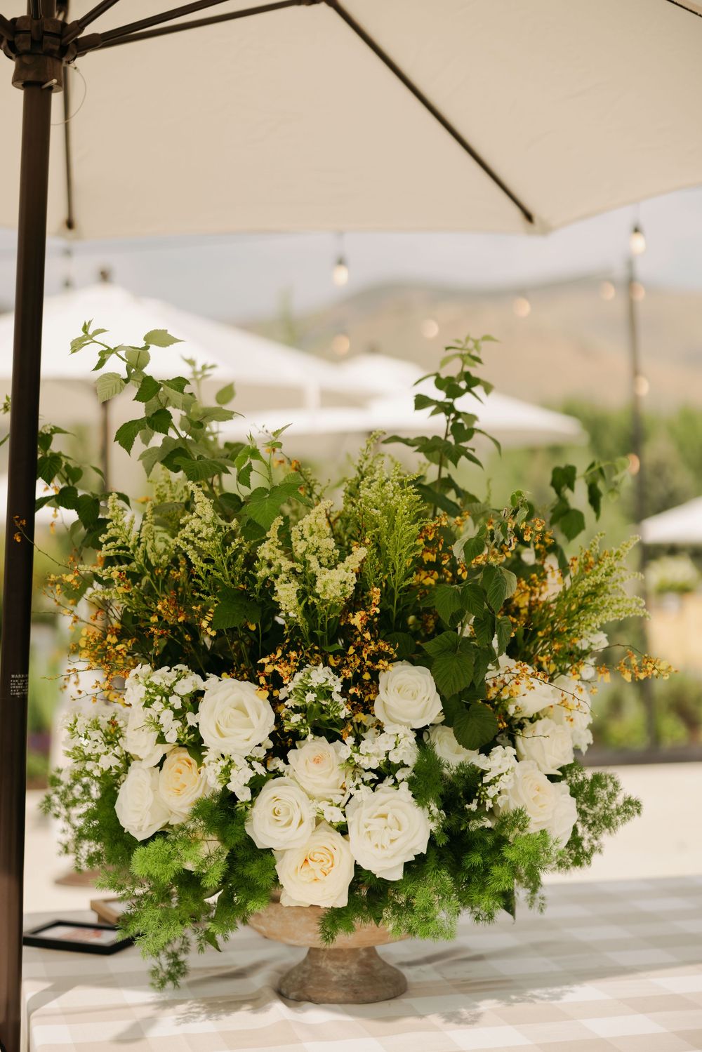 Elegant white floral centerpieces with roses and greenery arranged under a white tent for an outdoor wedding reception.