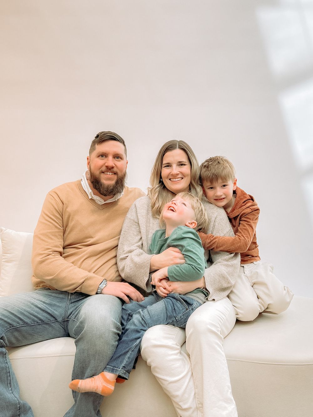 A family lounges together on a white couch, sharing smiles and embraces in a series of candid moments.