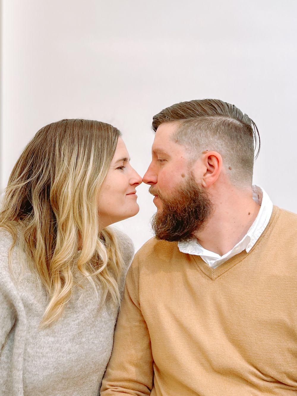 A couple in matching gray and tan sweaters share an intimate moment in a series of romantic poses.