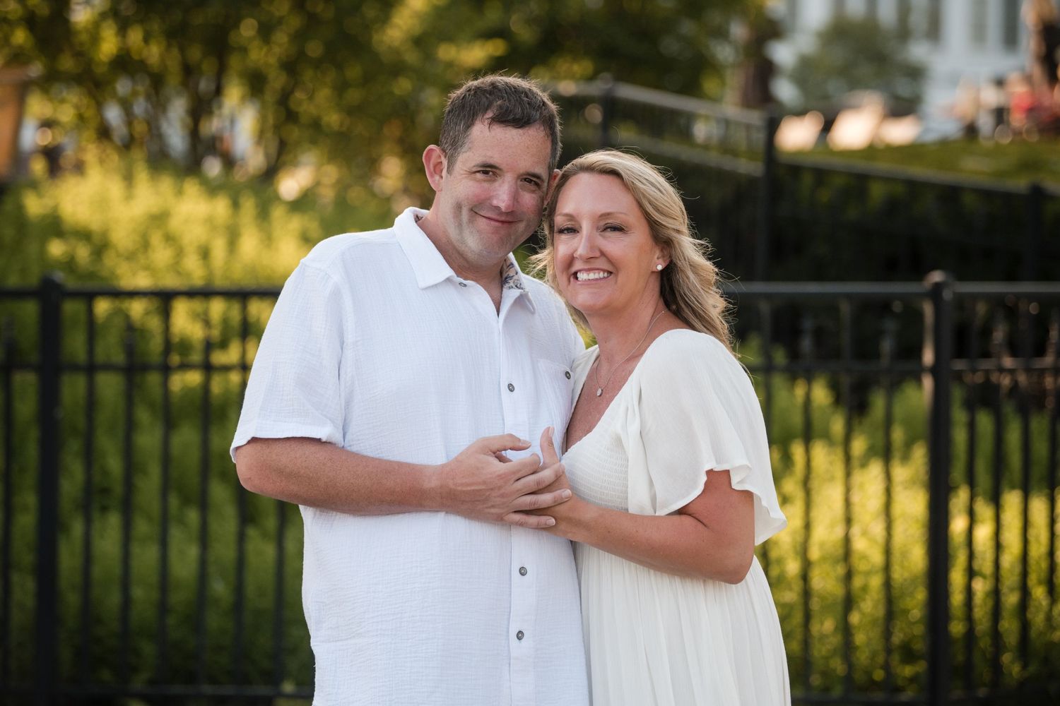 A couple in white outfits embrace and smile during an outdoor photo session at sunset.