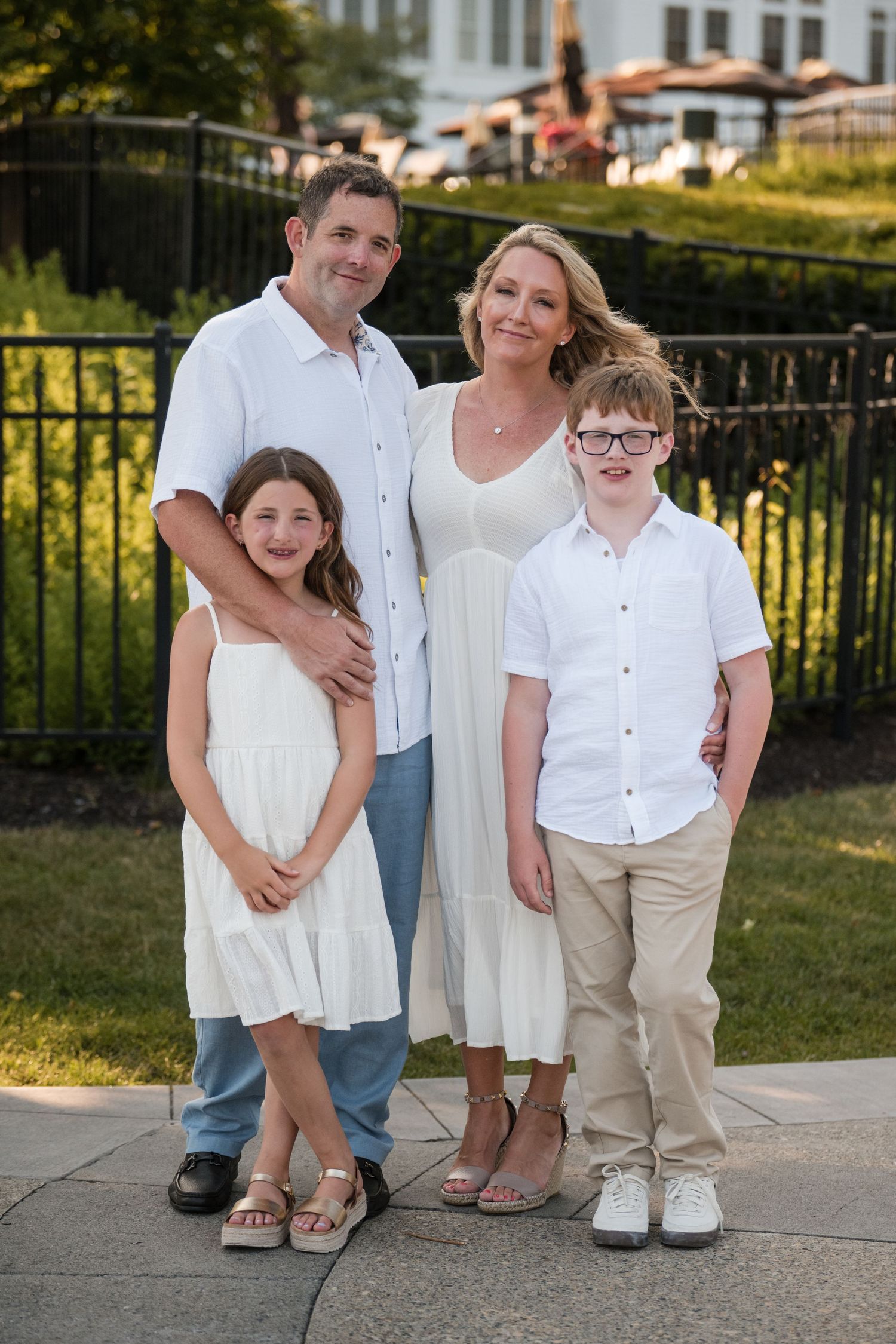 A family wearing coordinated white and beige outfits poses together outdoors in a series of casual portraits.