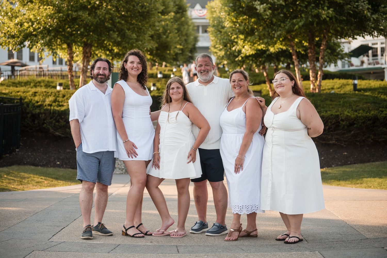 A group of people wearing white outfits pose together outdoors during a summer photo session.