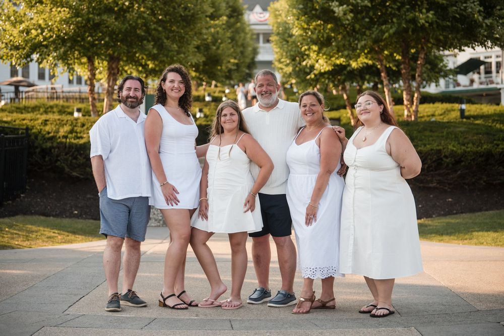 A group of people wearing white outfits pose together outdoors during a summer photo session.