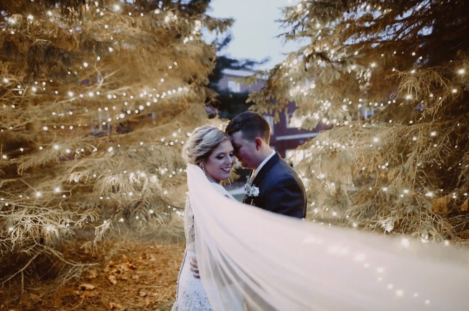 A romantic winter wedding moment captured with sparkling snowflakes and golden light in an outdoor setting.