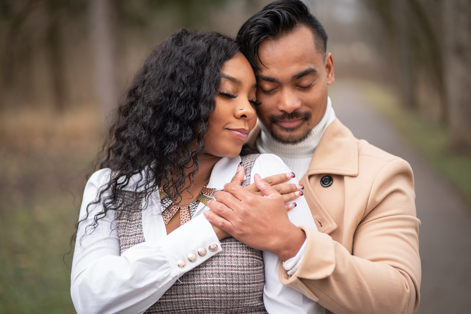 A couple in casual attire shares intimate moments during an engagement photoshoot in a natural setting.
