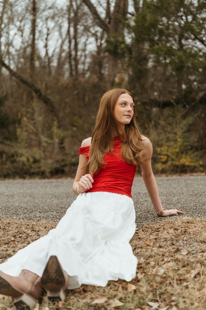 Figure in red and white outfit reclines on fallen leaves during an autumn photoshoot.