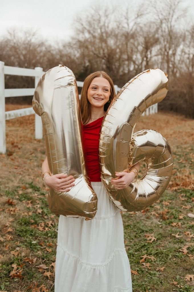 A person in a red top and white dress holds vintage cowboy boots in a fall outdoor setting.