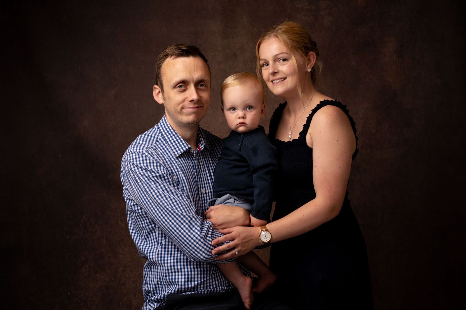 Studio portrait of a family of three against a dark brown background.