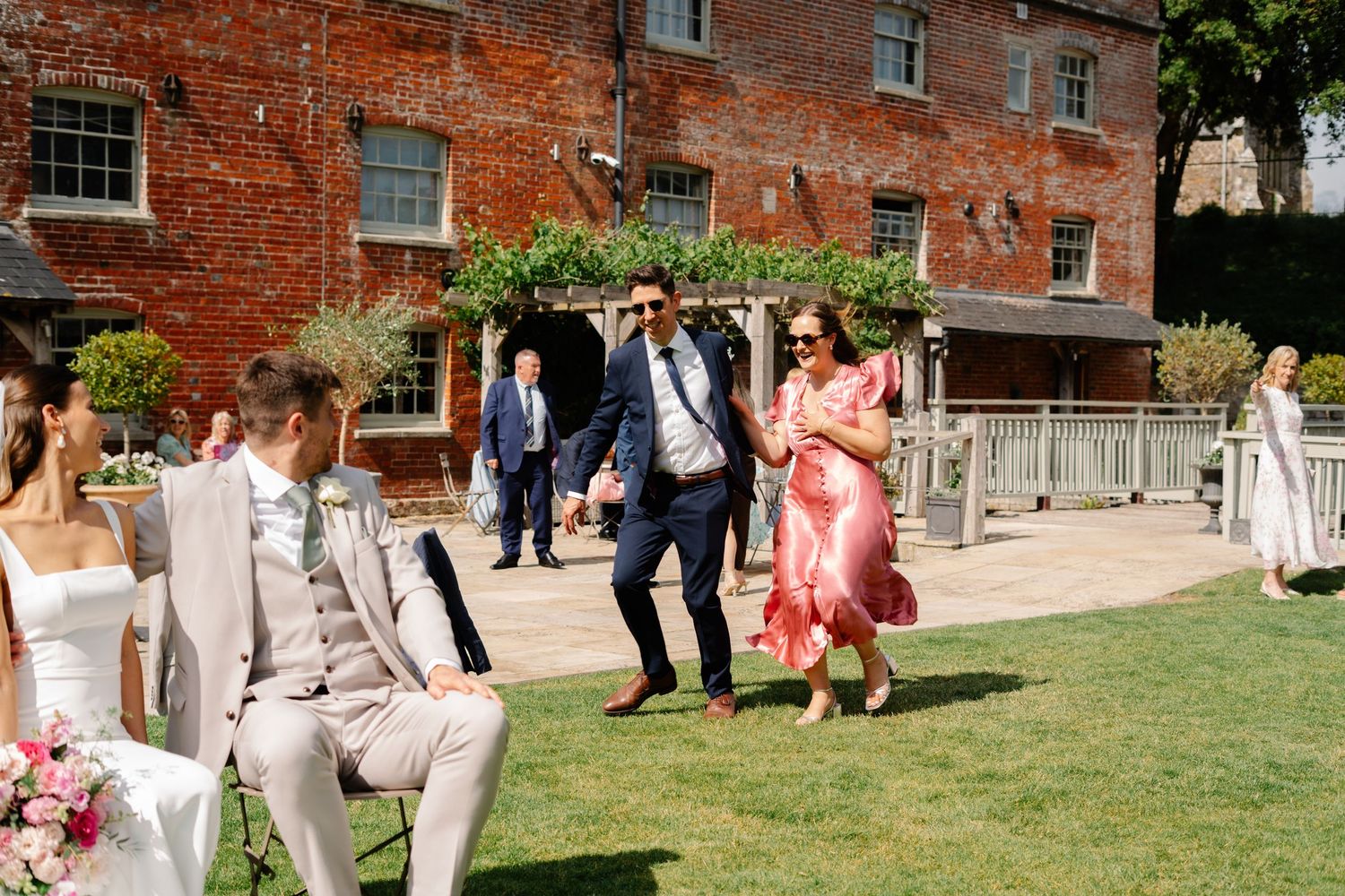 Couple sat waiting for photographs with guests running in enjoying photo roulette together at Sopley Mill