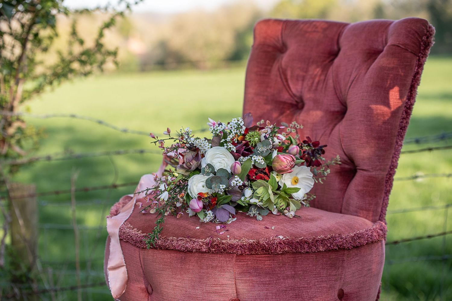 Bouquet of seasonal white and pink flowers rests on a pink chair, in front of a field