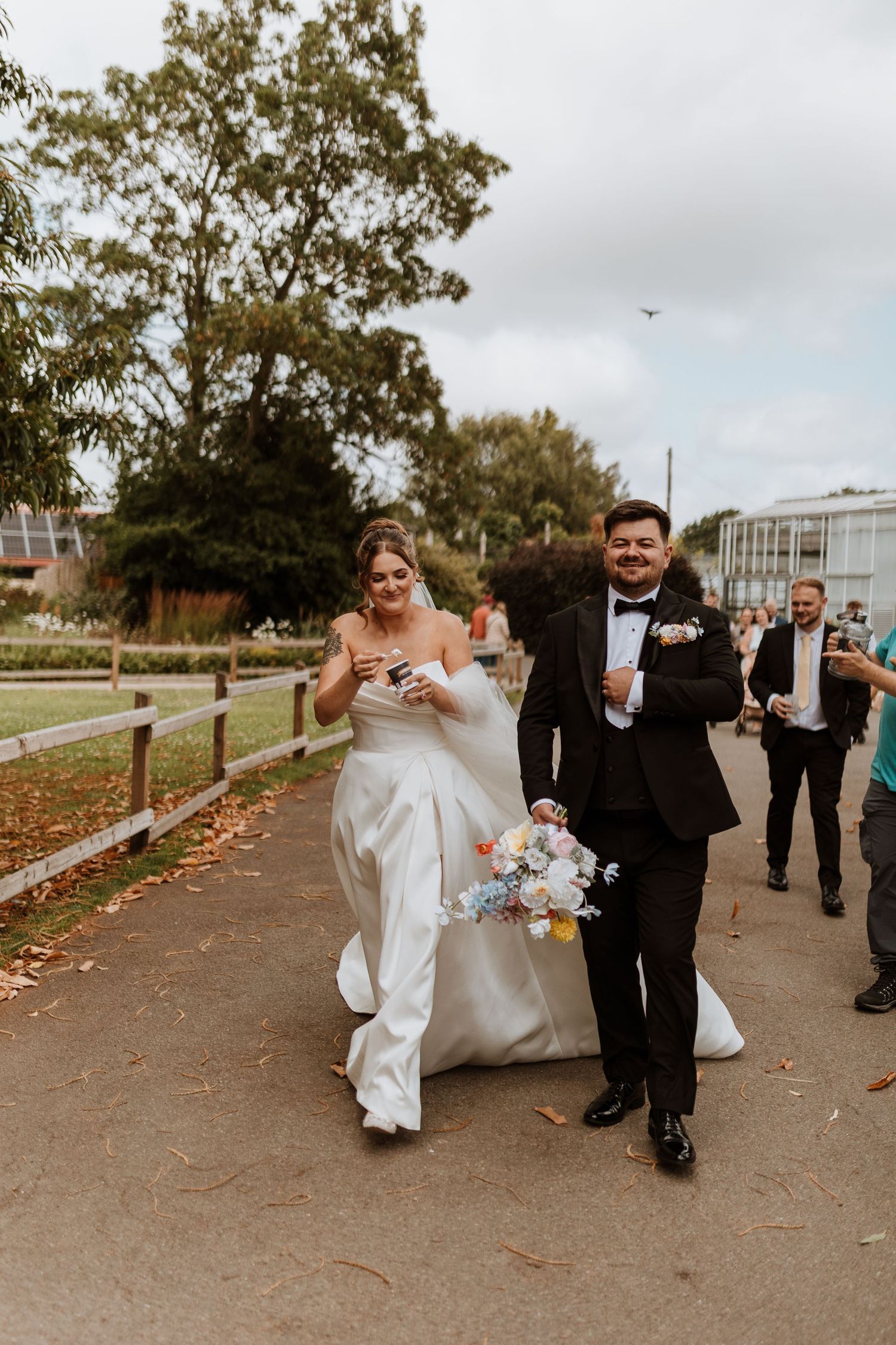 A bride and groom walk together eating icecream with wedding guests follow behind on zoo tour at Cheste Zoo