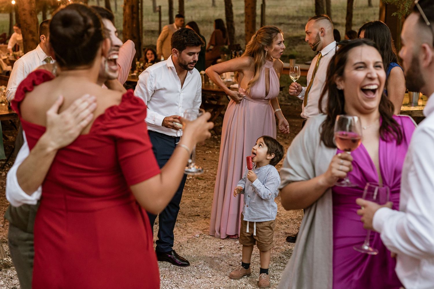 A group of people dance joyfully at an outdoor wedding reception during golden hour.