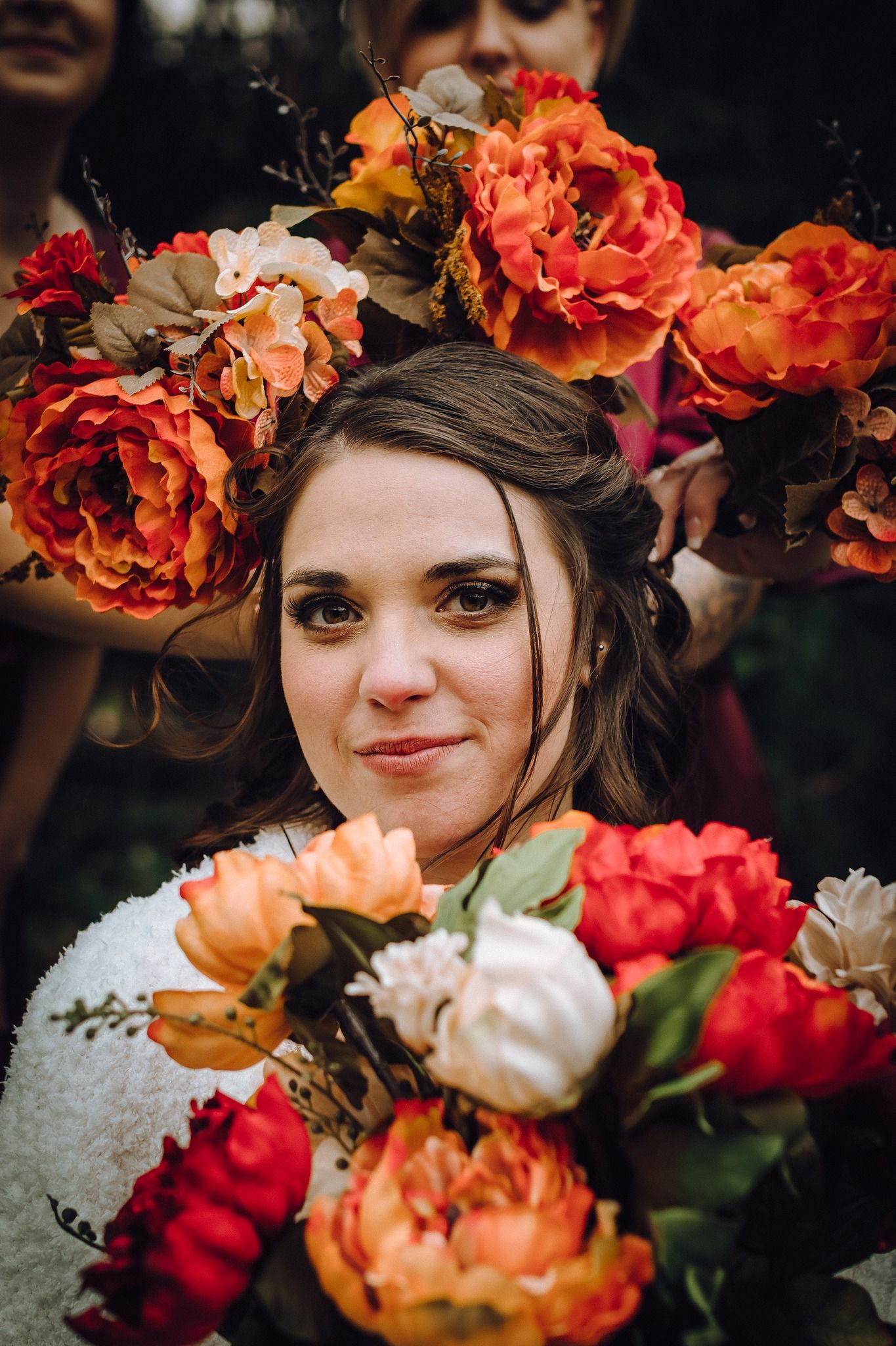 A floral crown made of vibrant orange and red blooms creates a romantic autumn-inspired look against a dark background.