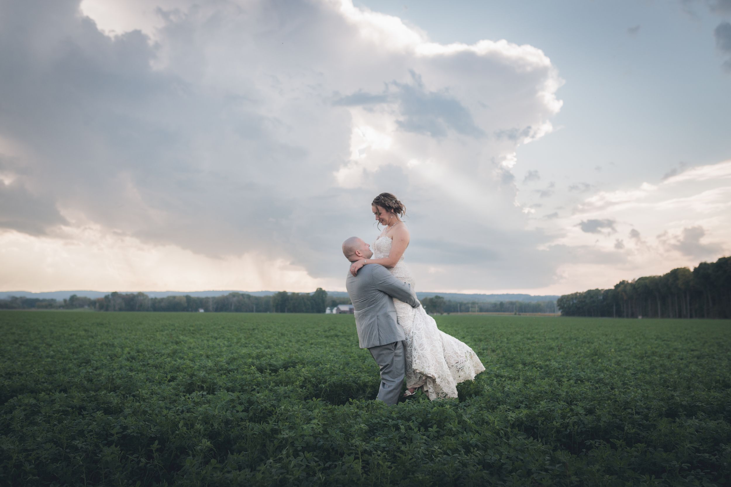 Romantic couple dancing in open green field during golden hour.