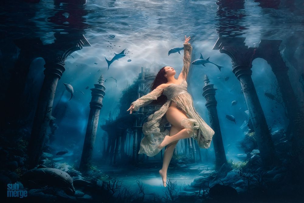 Ethereal underwater scene with a dancer in flowing white fabric surrounded by ancient ruins and swimming fish.