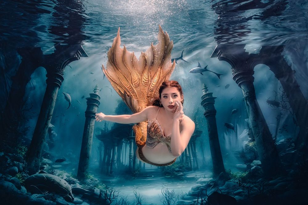 A mystical underwater scene with a mermaid swimming through dark blue waters surrounded by aquatic plants and light beams.