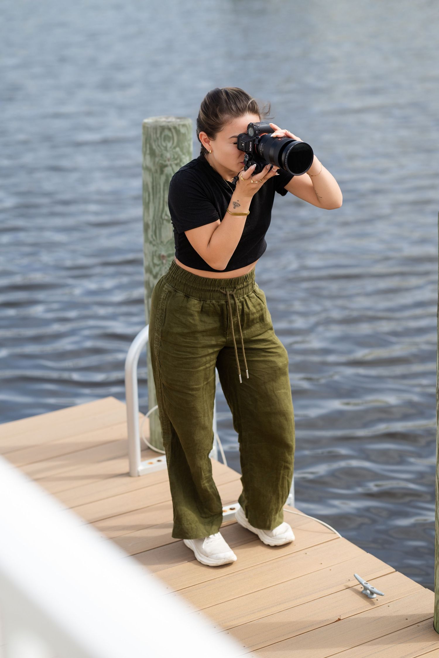 Photographer in olive pants crouching on a wooden dock to capture shots over water.