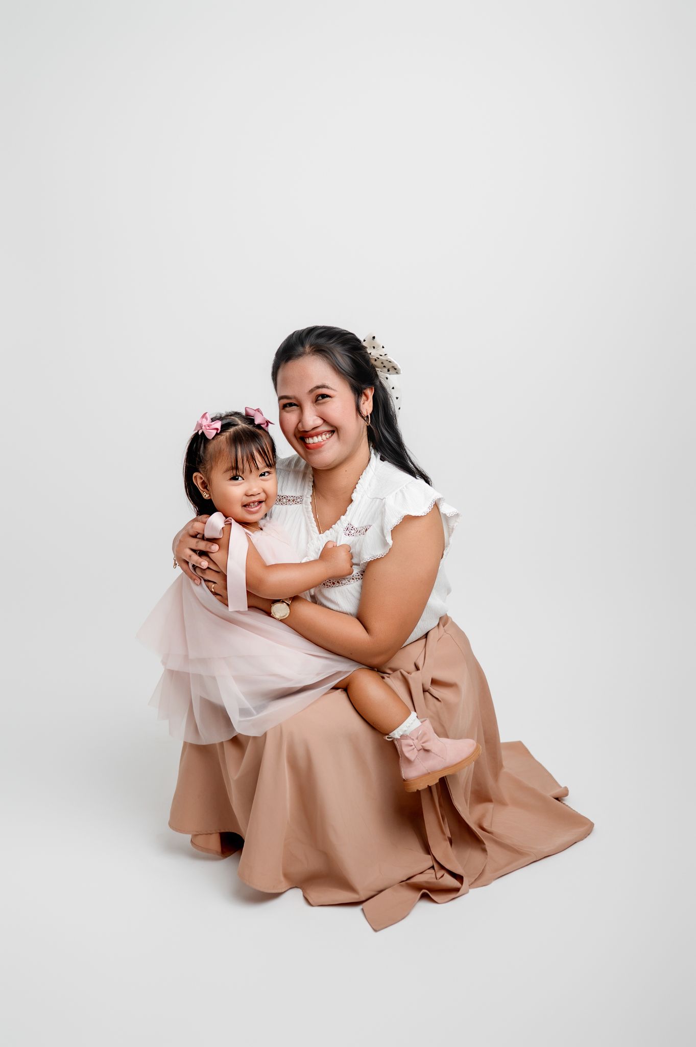 A mother and daughter in coordinating outfits share a joyful embrace against a white background.