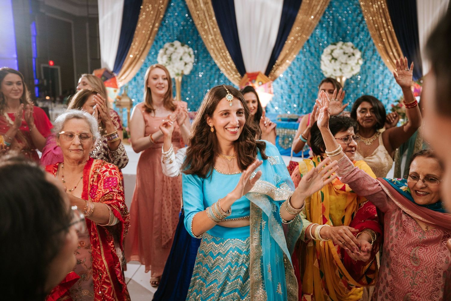 Wedding guests dance and celebrate on the dance floor at a vibrant Indian reception with traditional attire and decor.