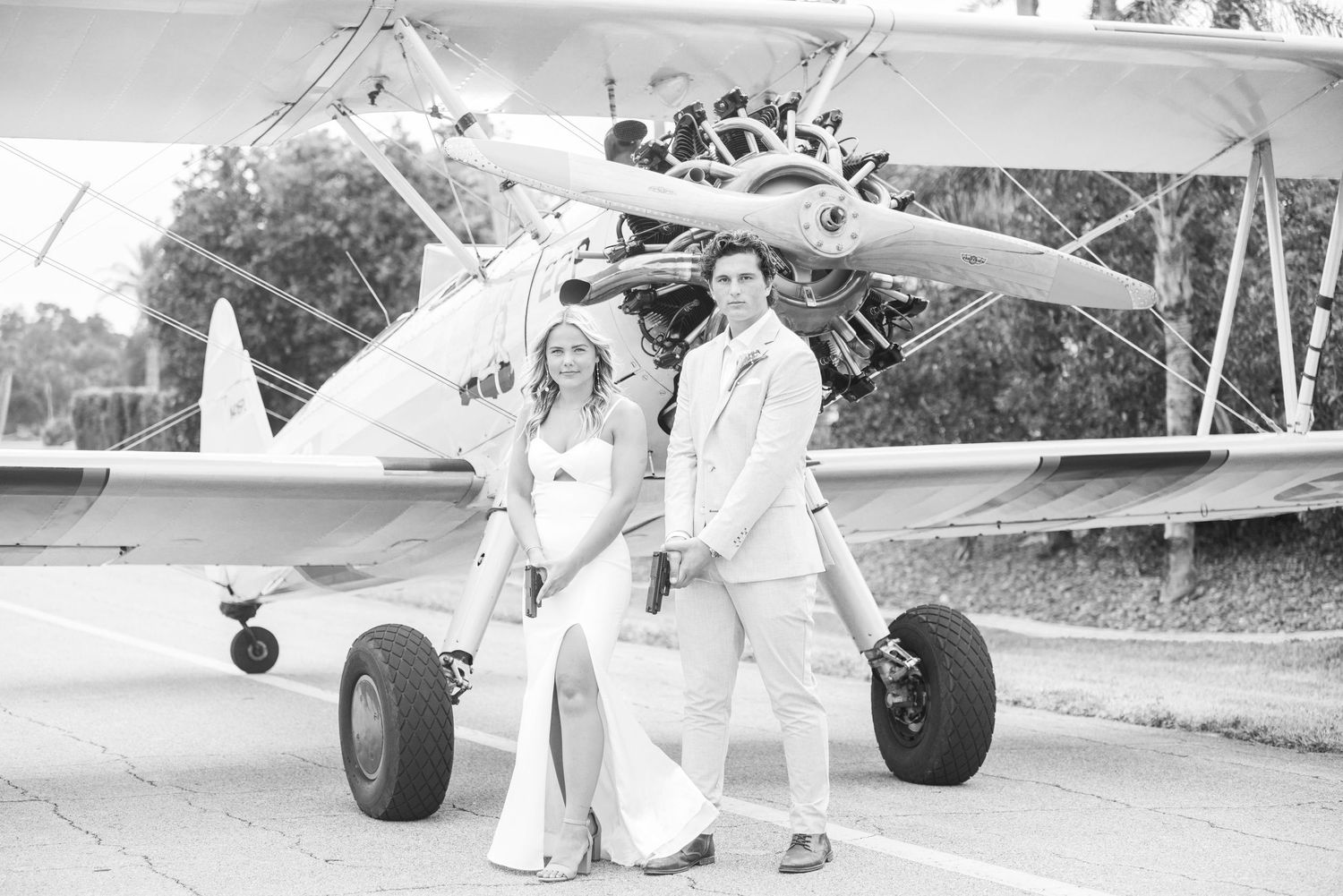 Couple in white outfits posing together in front of vintage biplane.