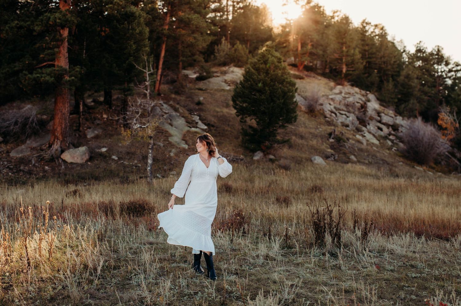 A couple in white wedding attire embraces in a scenic mountain landscape at sunset.