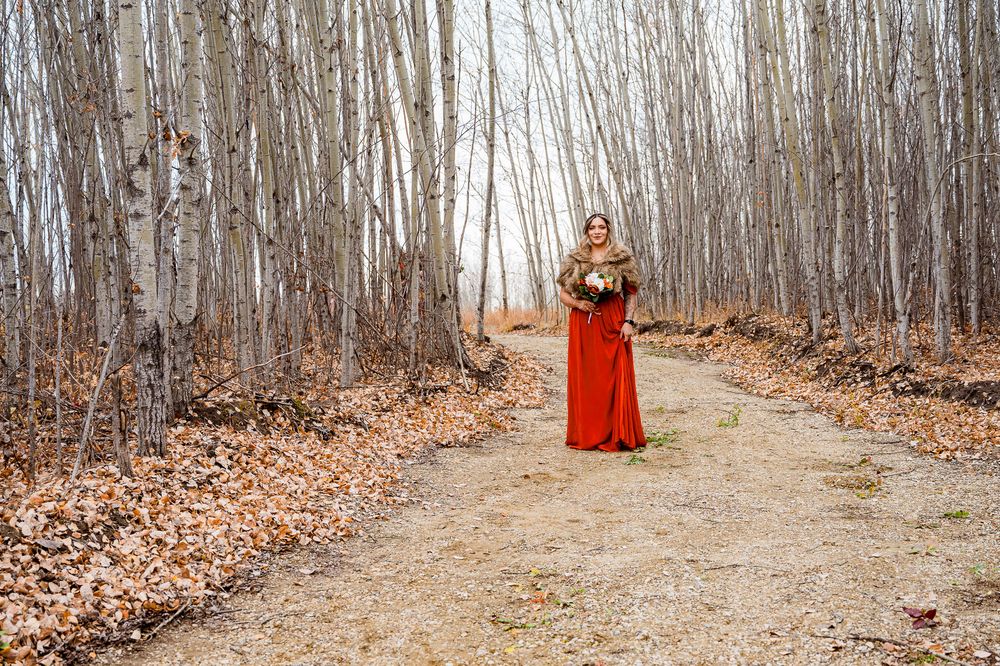 Woman in flowing red dress walks through autumn forest path covered in fallen leaves. parkland county wedding photographer, bridesmaid