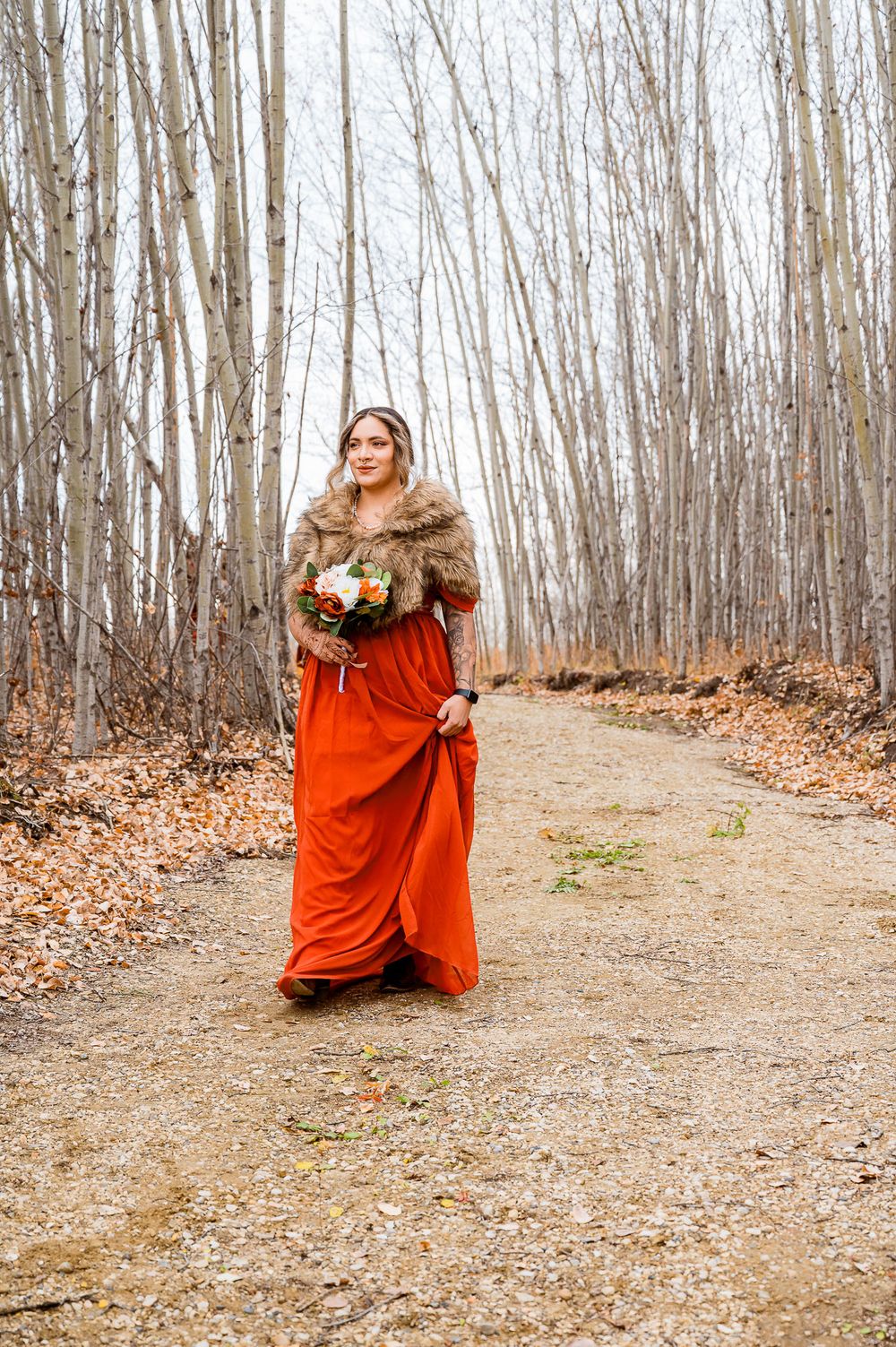 A figure in a flowing red dress dances gracefully through a bare winter forest with fallen leaves on the ground. parkland county