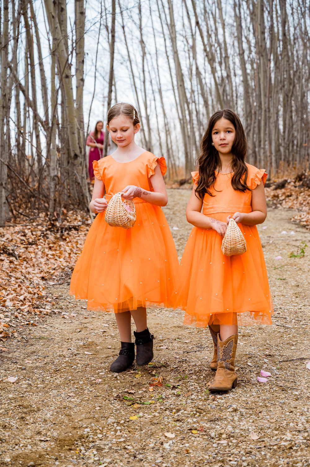 Young bridesmaids in bright orange tulle dresses walk through a wooded path holding wicker baskets. edmonton videographer