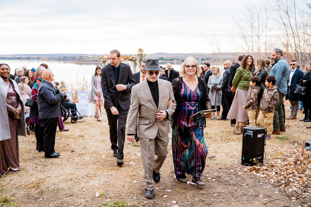 A group of people walk along a path near a lake during autumn with fallen leaves scattered on the ground. hand fasting ceremony