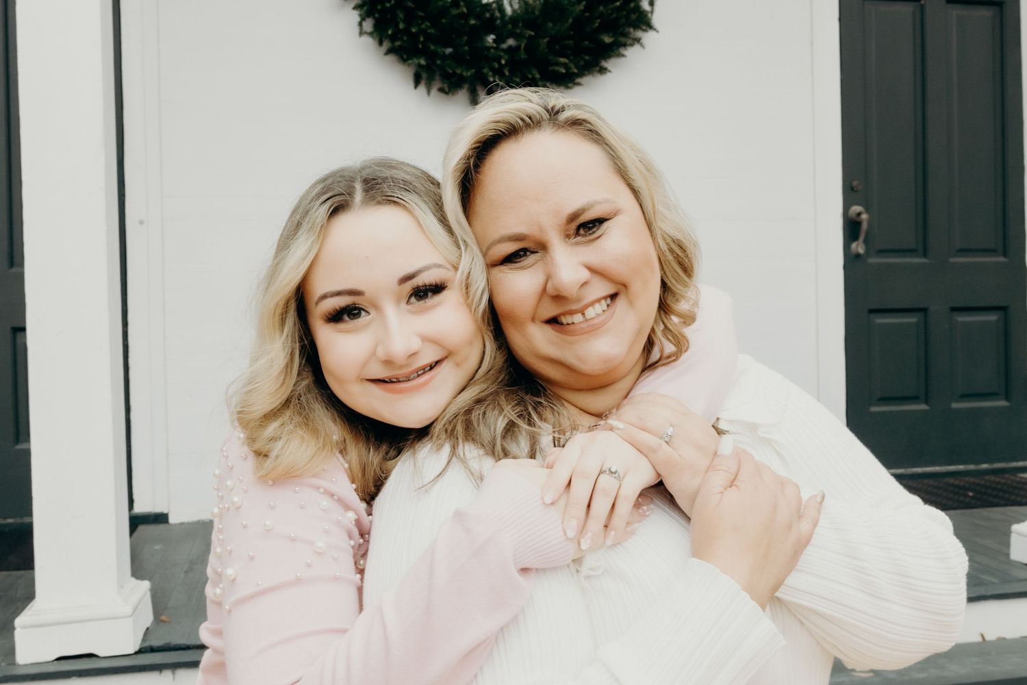 Two people in pink and white outfits posing together in front of a door with wreath.