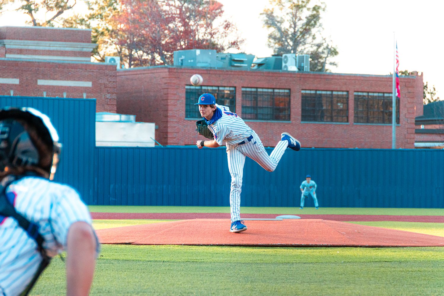 Baseball pitcher in blue uniform winds up to throw from the mound during a game at a baseball stadium.