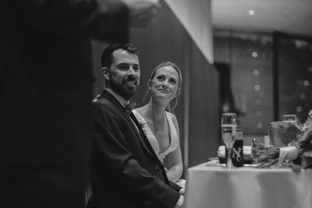 A black and white candid photo of a couple smiling together at a social gathering or event.