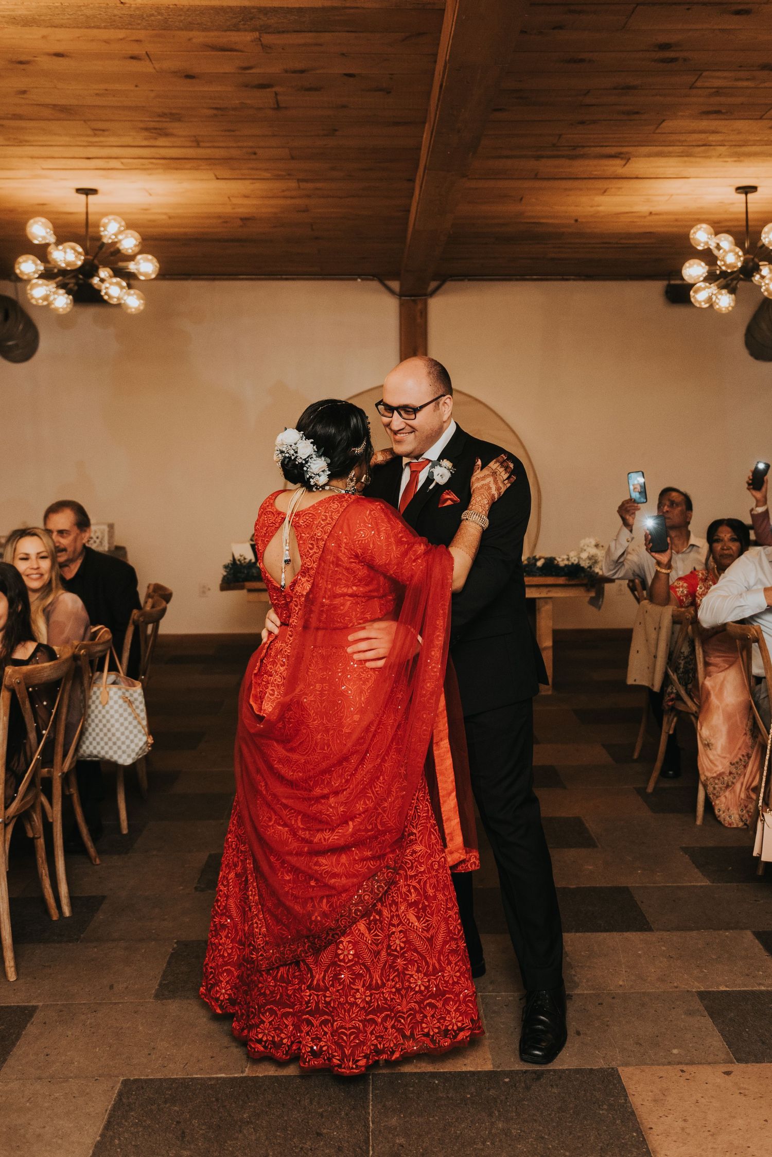A couple dances together at a wedding reception, with the person wearing a flowing red dress with intricate details.