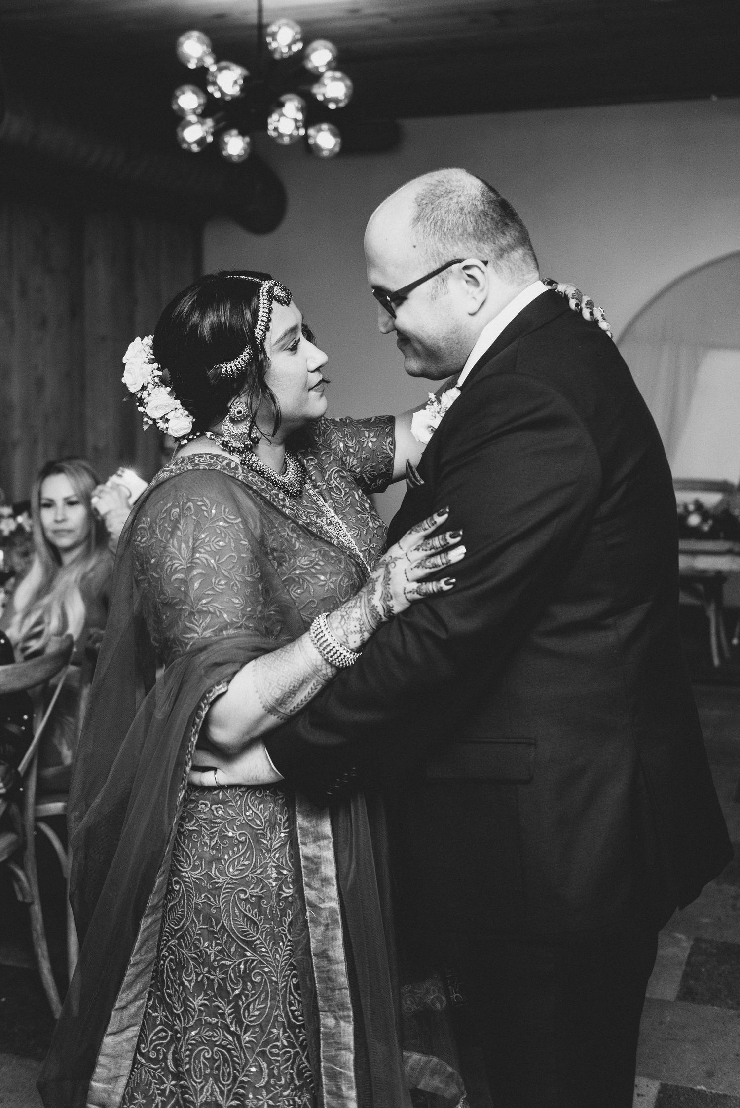 A couple shares an intimate dance moment in black and white at an indoor reception venue with ambient lighting.