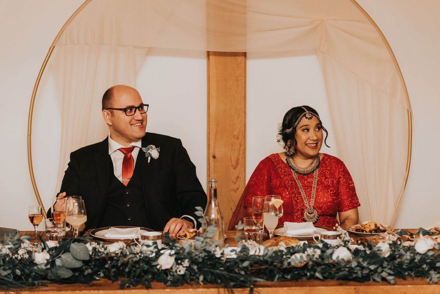 Wedding reception head table decorated with elegant greenery garlands and floral arrangements at a formal event.
